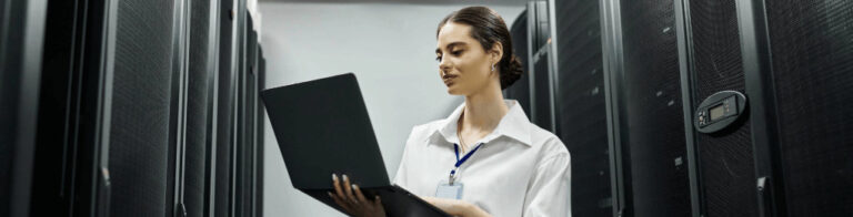 IT technician using a laptop by server racks